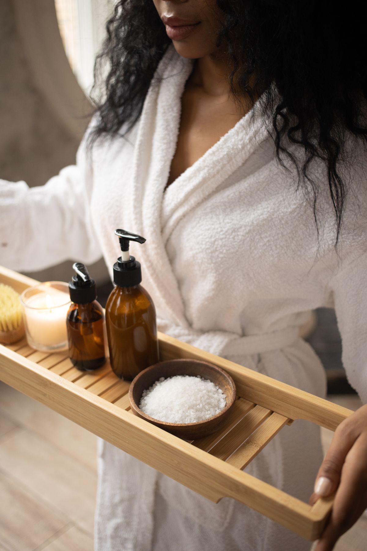 Aesthetician in a spa robe carrying a tray of skincare products